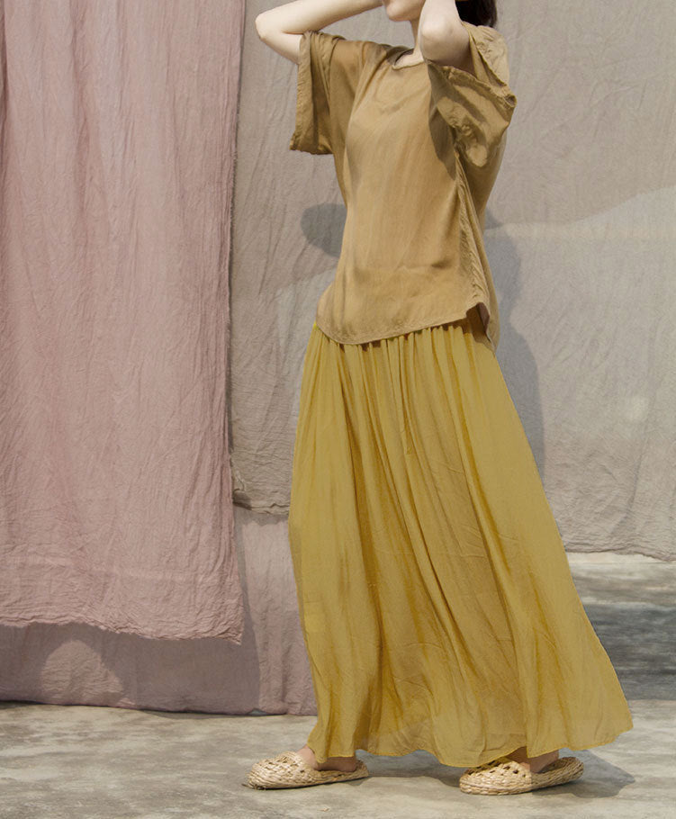 Gonna lunga a pieghe con vita elastica e orlo ampio, tessuto crepe de chine color zafferano, vestibilità fluida e elegante.