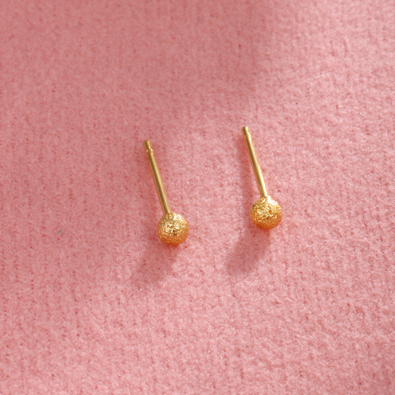 Piccoli orecchini a perno rotondi in oro placcato rame, finitura opaca e lucida, stile minimalista e raffinato.