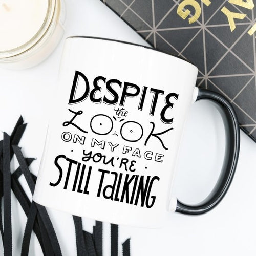 Tazza nera Sajishop con scritta "Despite The Look On My Face, You're Still Talking" in ceramica da 11 oz, dettaglio del manico.
